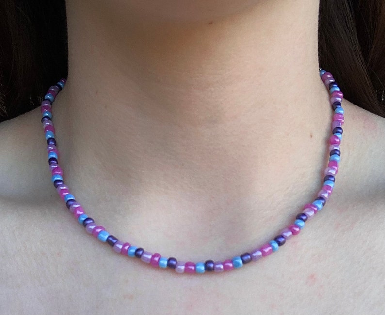May include: A delicate choker necklace made with small, iridescent beads in shades of pink, purple, and blue.