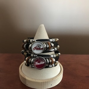 Könnte beinhalten: Drei Lederarmbänder mit Metallverzierungen und runden, bunten Logos. Die Logos zeigen die Worte "Indian Motorcycle" und "Since 1901".