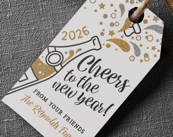 Peut inclure: Une bouteille de champagne avec une étiquette dorée et une étiquette cadeau attachée avec de la ficelle. L'étiquette indique "Cheers to the new year!" avec l'année 2026 et un graphisme festif en or et argent.