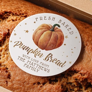 May include: A loaf of pumpkin bread in a cardboard box with a clear window. A round sticker on top reads "Fresh Baked Pumpkin Bread" with a pumpkin illustration and the family name. The bread has a golden-brown crust.