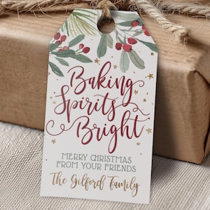 以下が含まれることがあります： バーガンディ色の筆記体で「Baking Spirits Bright」と書かれたギフトタグ。緑とベリーの水彩イラストで飾られています。タグは、ひもで包まれた茶色のパッケージに取り付けられています。