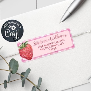 May include: A personalized address label featuring a watercolor strawberry and the name "Stephanie Williams." The label has a pink gingham border and includes the address: 1324 Magnolia Ave, Middletown, US 94900. A black circle with the text "Personalize with Corjl" is also visible.
