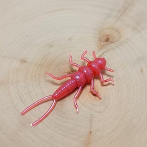 May include: A pink plastic fly fishing lure shaped like an insect.