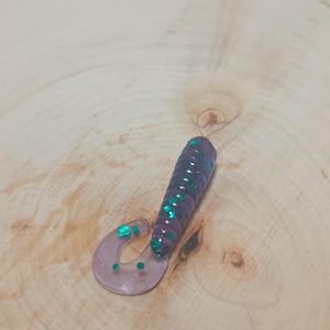 May include: A purple and green soft plastic fishing lure with a curled tail.