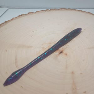 May include: A purple and green worm-shaped fishing lure with a speckled finish.