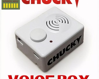 May include: A white rectangular voice box with the word "CHUCKY" printed in black on the side. The top features a speaker, a button, and a small red light. The words "VOICE BOX" are printed in red below.