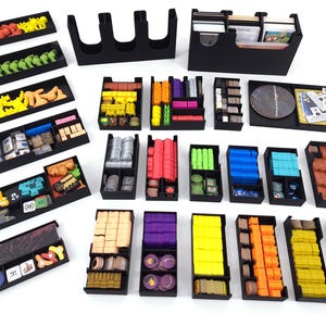Könnte beinhalten: Eine Sammlung von schwarzen Brettspiel-Organizern aus Kunststoff, gefüllt mit verschiedenen Spielkomponenten wie farbigen Holzwürfeln, Spielsteinen, Karten und Würfeln. Das Set enthält mehrere rechteckige Fächer in verschiedenen Größen, die zum Sortieren und Aufbewahren von Spielmaterial dienen.