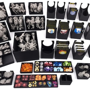 Könnte beinhalten: Eine Sammlung schwarzer Aufbewahrungsbehälter und -schalen, gefüllt mit Spielsteinen, Miniaturen und Karten. Die Miniaturen sind in verschiedenen Grautönen gehalten, und die Karten haben farbenfrohe Illustrationen. Die Spielsteine umfassen Würfel und Spielmarken.