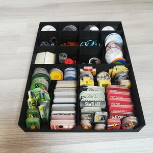 Puede incluir: Un organizador negro con m&uacute;ltiples compartimentos para guardar piezas de juego. Los compartimentos contienen varias cartas, fichas y dados. Las cartas tienen diferentes colores y dise&ntilde;os, incluyendo rojo, verde y amarillo. El texto en las cartas incluye "ALCOHOL", "COFFEE", "HEDDAI", "BROKEN GUITAR", "SHOVEL", "SAWBLADE", "KNIFE", "SHOTGUN", "PISTOL", "BOOK", "SHELL", y "WEAPON".