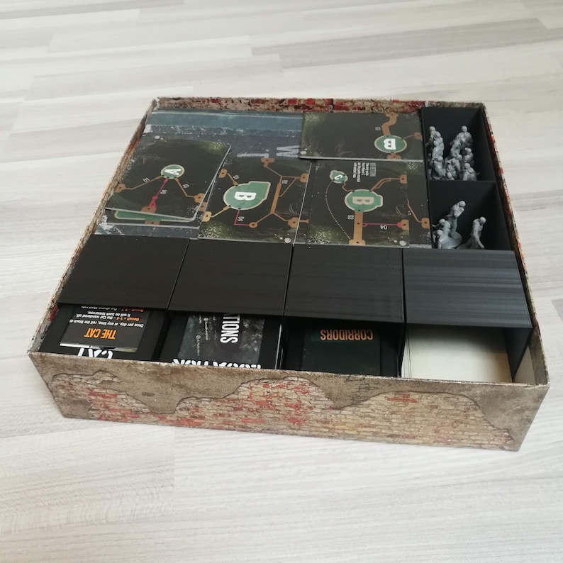 Puede incluir: Un inserto organizador negro para una caja de juego de mesa. El inserto tiene compartimentos para cartas, fichas y miniaturas. Los compartimentos est&aacute;n etiquetados como "Corridors", "Locations", "The Cat" y "Minions".