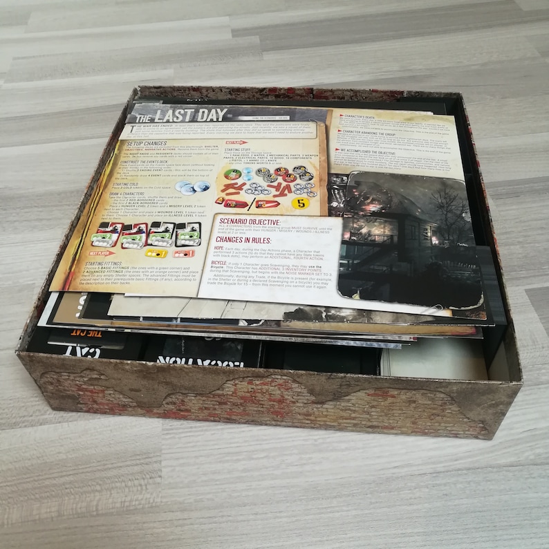 Puede incluir: La parte superior de una caja de juego de mesa con el t&iacute;tulo "The Last Day" impreso en la tapa. La caja est&aacute; abierta y las piezas del juego son visibles en el interior. Las piezas del juego est&aacute;n hechas de cart&oacute;n y pl&aacute;stico. El juego est&aacute; ambientado en un mundo postapocal&iacute;ptico.