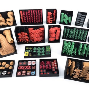 Puede incluir: Un conjunto de cajas de almacenamiento de plástico negro con varios compartimentos para organizar las piezas de juegos de mesa. Las cajas contienen una variedad de miniaturas de plástico, dados y fichas en colores rojo, verde, marrón y dorado.