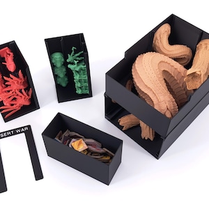 Puede incluir: Un conjunto organizador de juegos de mesa de plástico negro con varios compartimentos. Incluye una pieza plana con la etiqueta DESERT WAR, un contenedor con figuras rojas, uno con figuras verdes, una caja pequeña con fichas y una caja grande.