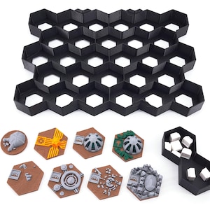 Könnte beinhalten: Ein schwarzes sechseckiges Fliesenraster mit 25 sechseckigen Feldern. Es gibt acht sechseckige Spielsteine mit verschiedenen Designs, darunter ein gelbes und oranges Stück mit einem Sonnensymbol, ein graues Stück mit einer Kuppel und ein grünes Stück mit einem Baum. Es gibt auch einen schwarzen sechseckigen Behälter mit weißen Würfeln.
