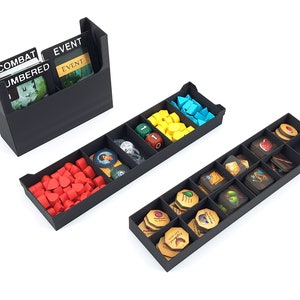 Op de afbeelding: Zwarte plastic organizer met vakken om spelstukken en kaarten op te bergen. De organizer heeft vakken voor rode hartvormige tokens, gele en blauwe plastic stukken, dobbelstenen en kaarten met de woorden "Event" en "Combat Numbered".