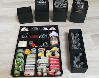 May include: A black organizer with multiple compartments for storing game pieces and cards. The organizer has a black and white label that says "SEWERS". The organizer is filled with various game pieces, including cards, tokens, and dice.