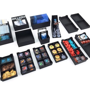 May include: Black plastic organiser trays for board game components. The trays are filled with various game pieces, including cards, tokens, and dice. The trays are labelled with the names of the game components, such as "Adventure", "Quest", and "Enemy Buff".