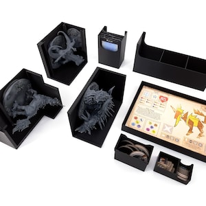 Op de afbeelding: Zwarte plastic organizerset voor een bordspel. De set bevat een dienblad met vakken voor tokens, een kaarthouder en verschillende dozen voor het opbergen van miniaturen. Het dienblad heeft een gedrukt speelbord met het nummer 85.