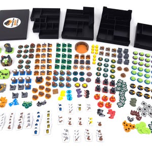 Könnte beinhalten: Ein Brettspiel-Organizer-Set mit vier schwarzen Kunststoffschalen und einem schwarzen Deckel mit einem runden Aufkleber mit der Aufschrift Ticketing Paw Root 3D Tokens, begleitet von einer Vielzahl kleiner, bunter 3D-gedruckter Spielsteine.