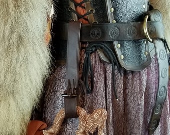 May include: A brown leather strap with a metal buckle is attached to a ceramic mug with a dragon design. The mug has a picture of a dragon in a fiery landscape.
