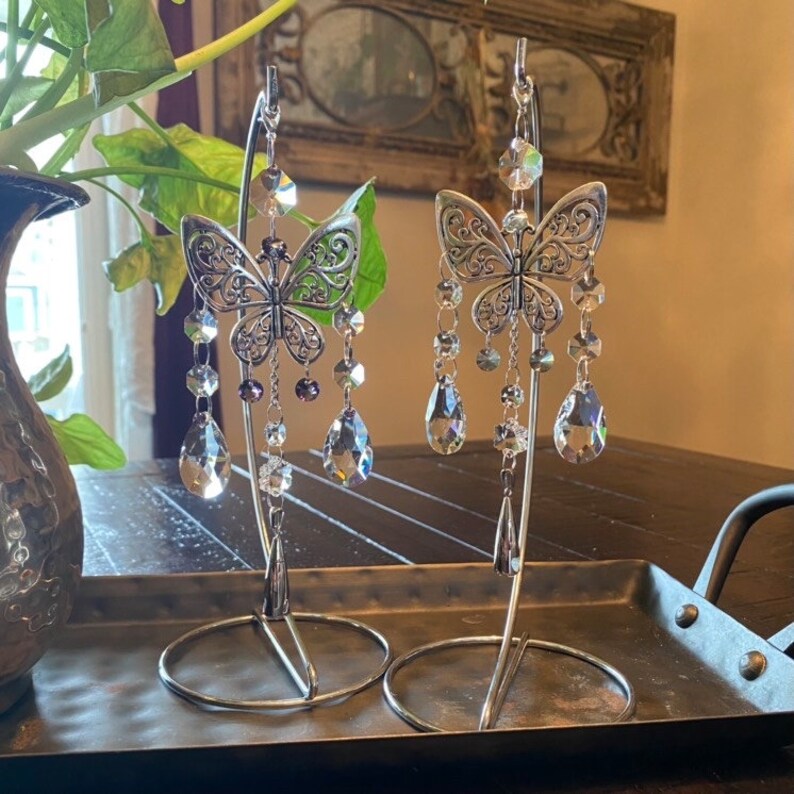 May include: Two silver butterfly-shaped crystal suncatchers hanging from metal stands. Each suncatcher features a detailed butterfly design with dangling crystal beads and teardrop-shaped crystals.