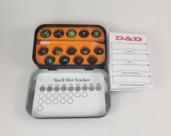 May include: A metal tin with a black lid and a white label that says "Spell Slot Tracker". The tin has 18 small compartments, each containing a small green and black dice. The tin is open and the compartments are visible. There is a pencil in the tin. There is a white sheet of paper with the text "D&D" in red and black, and the text "Name", "Race", "Class/Level/Exp", and "Alignment/Background" in black.