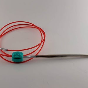 May include: A red circular knitting needle with a turquoise plastic connector. The needle is made of metal and is approximately 10 inches long.