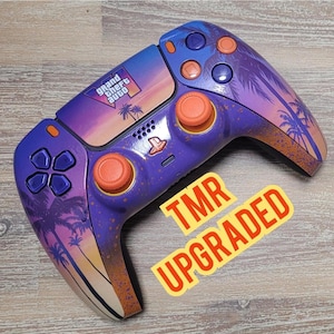May include: A wireless video game controller featuring a purple and orange sunset gradient with palm tree silhouettes and the Grand Theft Auto logo on the touchpad. The controller includes orange analog sticks and a yellow sticker reading TMR UPGRADED.