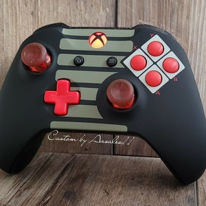 May include: Black Xbox controller with red and olive green accents. Features red buttons, thumbsticks, and a directional pad. The controller has a custom design with the text "Custom by Aasales!!".