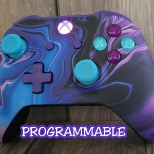 May include: An Xbox controller with a custom design. The controller has a swirling pattern of blue, purple, and black. The buttons are teal and purple. The word "PROGRAMMABLE" is written across the bottom.