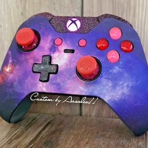 May include: Customized Xbox controller with a galaxy design. The controller features a purple and blue nebula pattern, red thumbsticks, and pink buttons. The text "Custom by Aasales!!" is written on the controller.