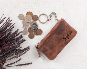 May include: A brown leather coin purse with a zipper closure and a silver key chain. The purse has the name "Sophia" engraved on it.