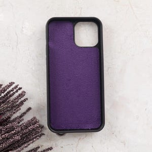Puede incluir: Una funda de tel&eacute;fono rectangular con marco negro y un forro interior de tela texturizada de color morado intenso. La funda presenta un gran recorte cuadrado en la esquina superior derecha para el m&oacute;dulo de la c&aacute;mara y esquinas redondeadas.