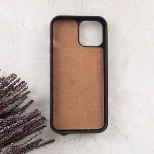 Puede incluir: Una funda rectangular para smartphone con un marco negro y una incrustaci&oacute;n texturizada de color tostado, similar al ante, en la parte posterior. La funda incluye un gran recorte cuadrado en la esquina superior derecha para la c&aacute;mara.