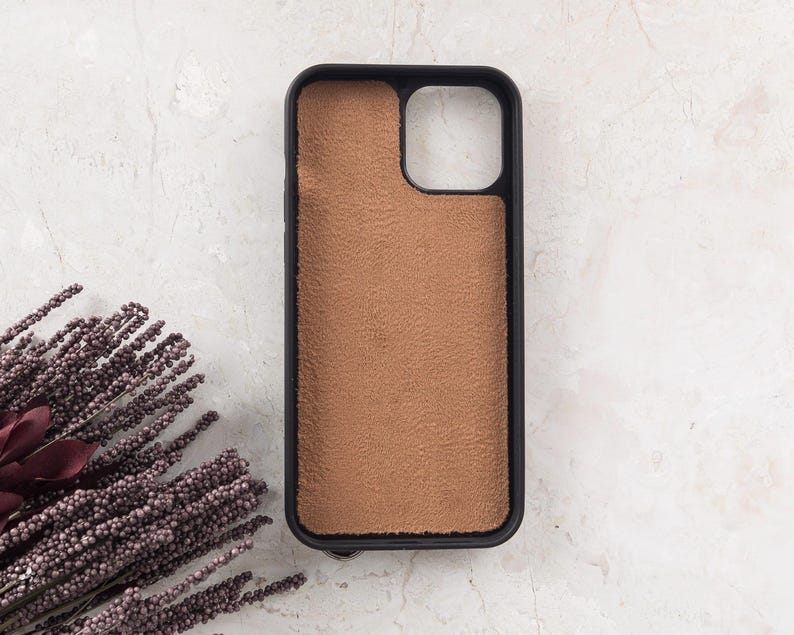 Puede incluir: Una funda rectangular para smartphone con un marco negro y una incrustaci&oacute;n texturizada de color tostado, similar al ante, en la parte posterior. La funda incluye un gran recorte cuadrado en la esquina superior derecha para la c&aacute;mara.