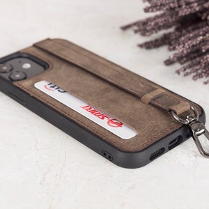 Puede incluir: Una funda de tel&eacute;fono de cuero marr&oacute;n con marco negro, que incluye una ranura para tarjetas con una tarjeta Citi y una tarjeta SMRT. La funda cuenta con una correa de cuero vertical sujeta a un mosquet&oacute;n de metal oscuro para el agarre.