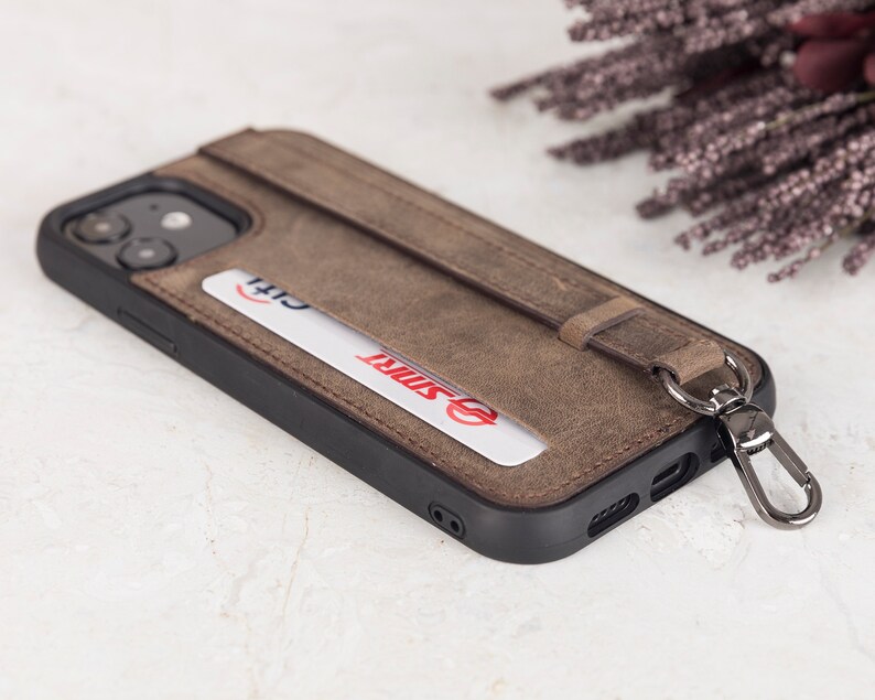 Puede incluir: Una funda de tel&eacute;fono de cuero marr&oacute;n con marco negro, que incluye una ranura para tarjetas con una tarjeta Citi y una tarjeta SMRT. La funda cuenta con una correa de cuero vertical sujeta a un mosquet&oacute;n de metal oscuro para el agarre.