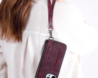 Peut inclure: Une coque de téléphone bordeaux foncé avec une fente verticale pour carte et une dragonne assortie détachable. La coque présente une finition mate, un cadre noir autour des objectifs de l'appareil photo et un fermoir métallique argenté.