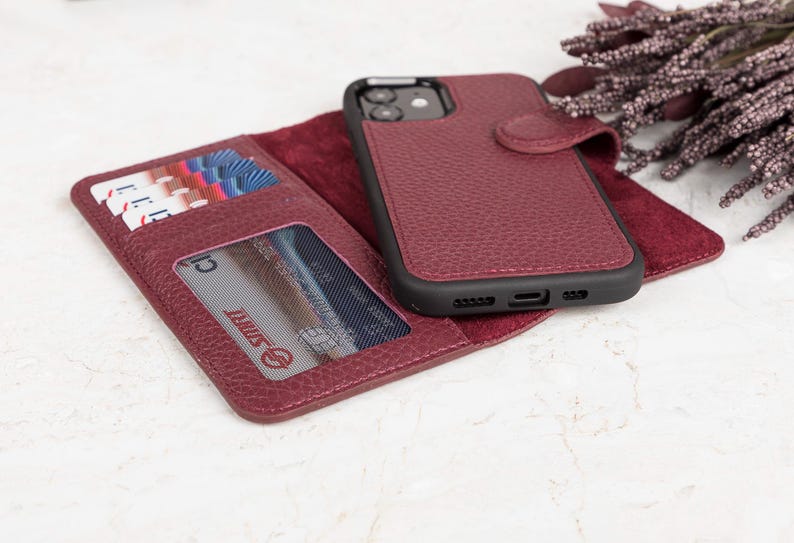 May include: A burgundy textured wallet phone case with a magnetic closure, featuring an integrated smartphone holder, multiple card slots, and a clear ID window. The interior is lined with a soft burgundy material, and the exterior has a pebbled finish.