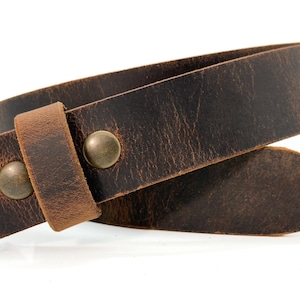 May include: A dark brown leather belt featuring a distressed, textured finish and a pointed tip. The belt is secured with two round, antique brass-colored metal rivets that hold the leather loop in place against the main strap.