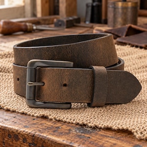 May include: A dark brown leather belt with a distressed, matte finish and a rectangular, dark metal buckle. The belt features a single leather keeper loop and several punched holes for adjustment, showcasing a rugged, textured surface.