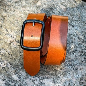 A tan leather belt with a black metal buckle. The belt is folded in half and the buckle is visible.