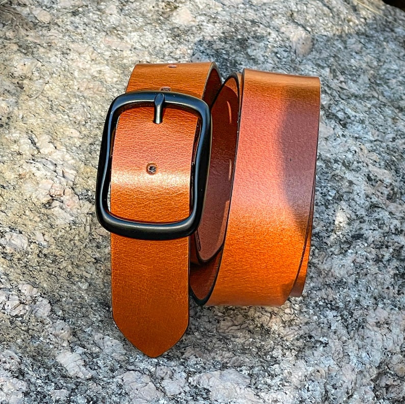 A tan leather belt with a black metal buckle. The belt is folded in half and the buckle is visible.