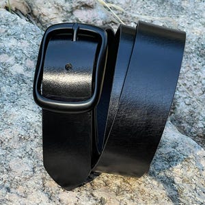 A black leather belt with a black metal buckle. The belt is rolled up and the buckle is visible.