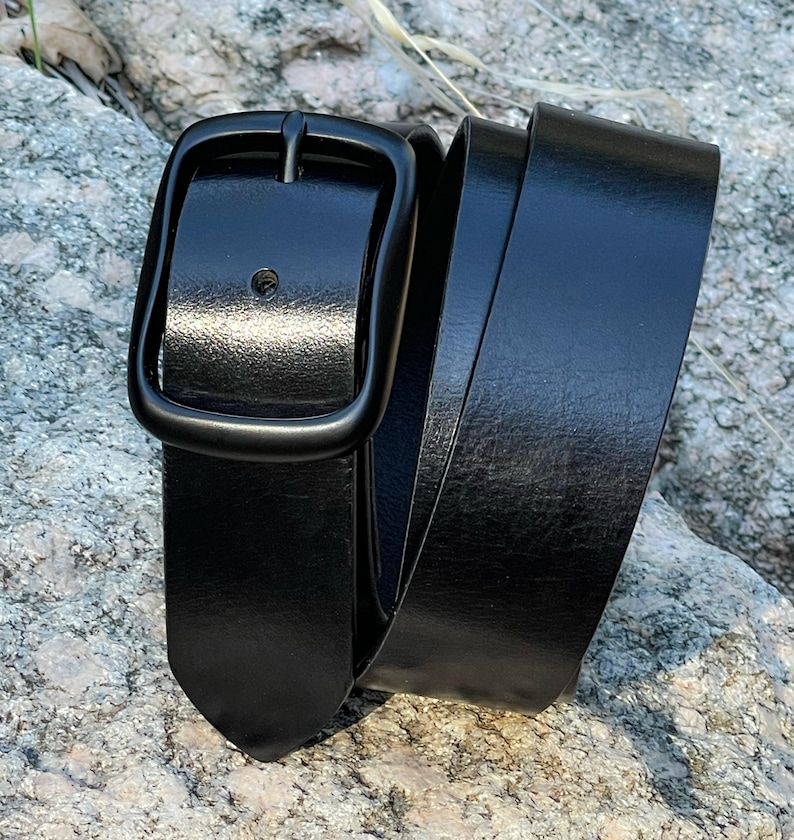 A black leather belt with a black metal buckle. The belt is rolled up and the buckle is visible.