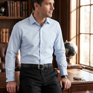 Pode incluir: Uma camisa de manga comprida azul-clara com colarinho cl&aacute;ssico e punhos, combinada com cal&ccedil;as pretas e um cinto de couro preto texturizado com fivela prateada. A camisa est&aacute; metida para dentro das cal&ccedil;as, criando um visual formal.