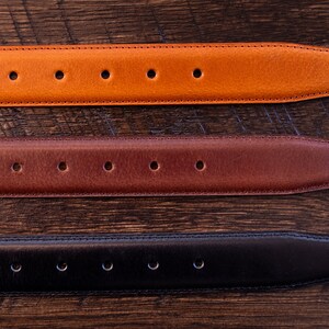 May include: Three leather belt straps arranged horizontally, featuring a tan, a medium brown, and a black option. Each strap has a tapered end, a series of evenly spaced circular adjustment holes, and visible stitching along the edges.