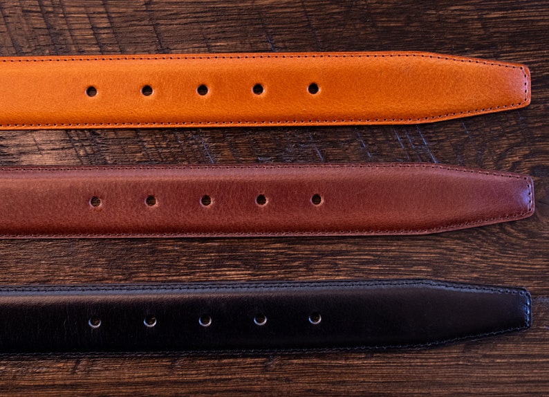May include: Three leather belt straps arranged horizontally, featuring a tan, a medium brown, and a black option. Each strap has a tapered end, a series of evenly spaced circular adjustment holes, and visible stitching along the edges.