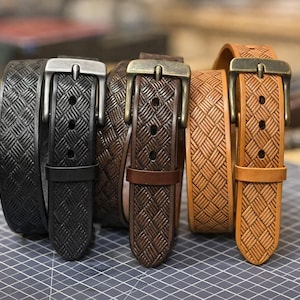 May include: A collection of leather belts in various shades of brown and black. Each belt features a woven pattern and a metal buckle. The belts are arranged on a gray surface, showcasing their different colors and textures.