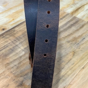 May include: A dark brown leather belt with a distressed, textured finish. The belt features a rounded tip and a series of five evenly spaced circular holes punched along the center for adjustment, showcasing the natural grain of the material.